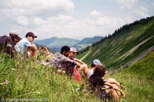 Campers sitting on a grassy slope taking in the view over the alpine valley