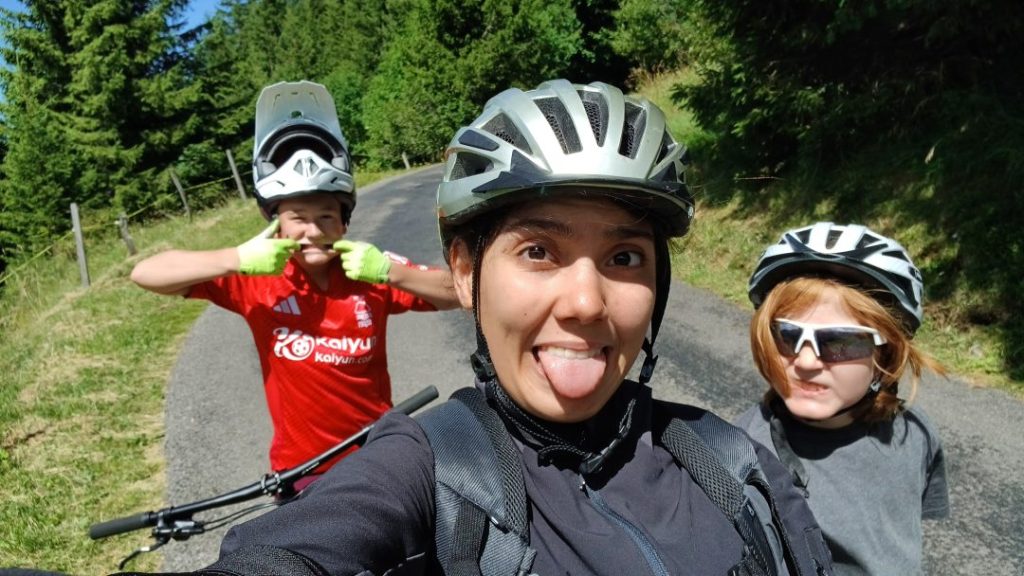 Moniteur de VTT et deux campeurs casqués sur une route forestière dans les Alpes