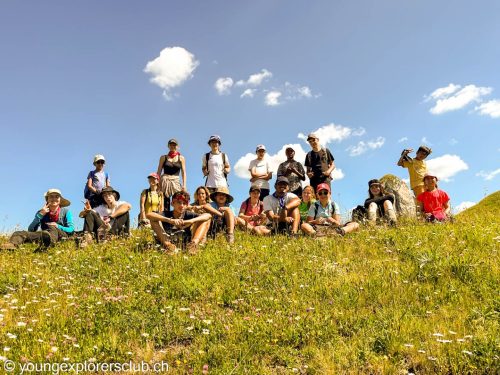 Large group of campers posing on a grassy hilltop under a summer sky