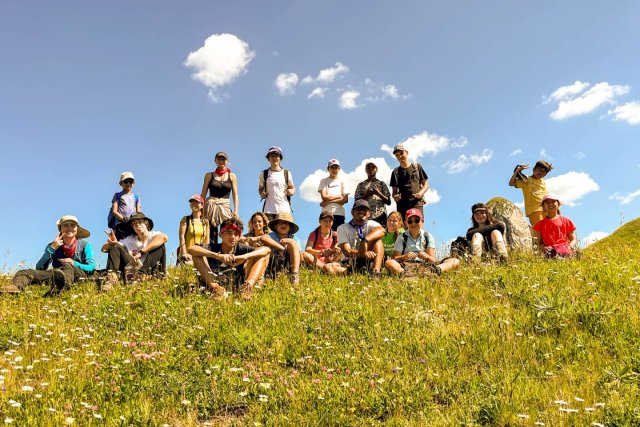 Large group of campers posing on a grassy hilltop under a summer sky