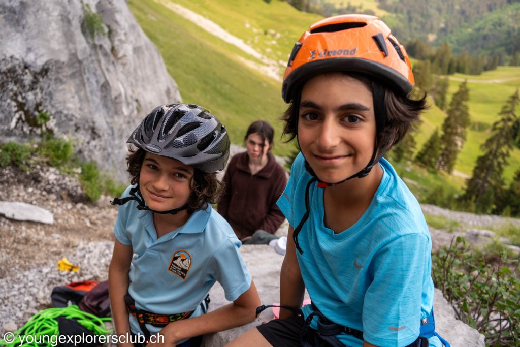 Two young climbers in helmets smiling at the foot of the rock face in Les Diablerets