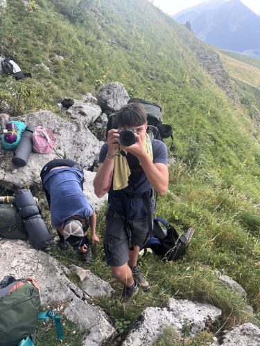 Staff member photographing hikers resting with their backpacks on a rocky alpine slope