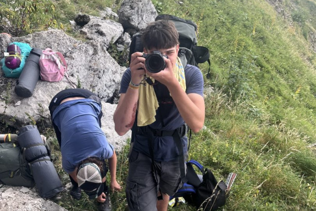 Staff member photographing hikers resting with their backpacks on a rocky alpine slope