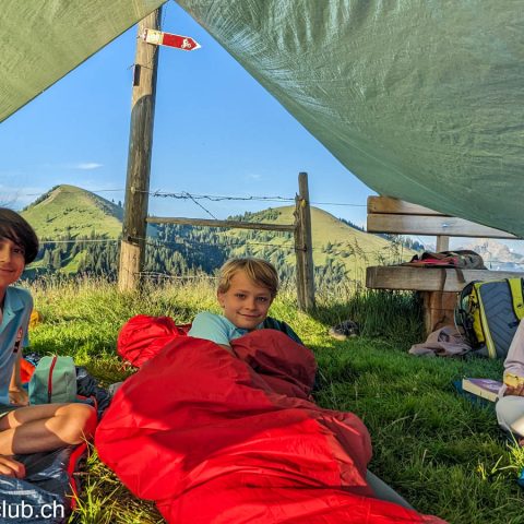 Campers in sleeping bags under a tarp shelter they built at the Survival Academy summer camp