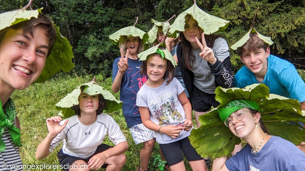 Campers and a counsellor wearing giant leaves as hats during a forest walk at summer camp