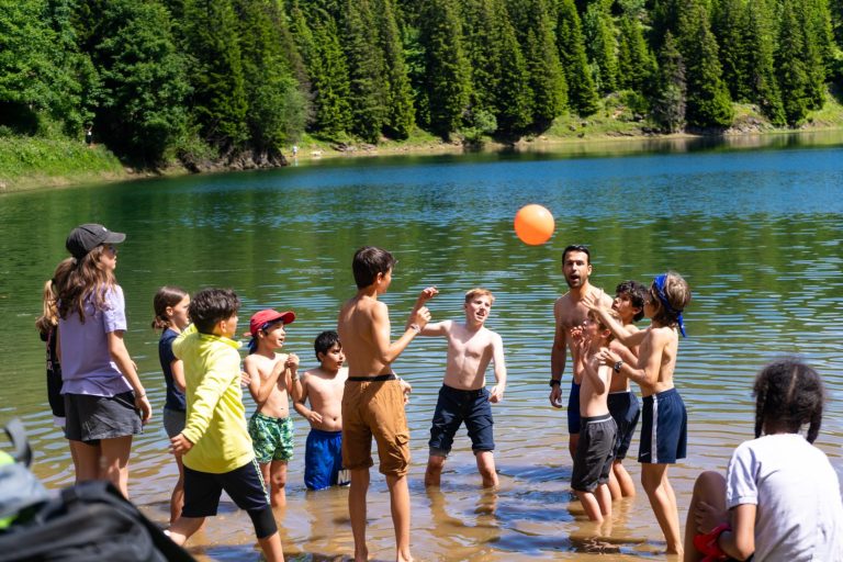 Campistas jugando a la pelota en un lago de montaña rodeado de abetos