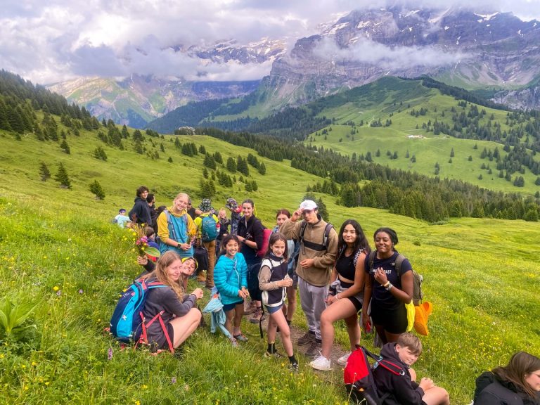 Campers relaxing in a green alpine meadow below the cliffs on the Adrenaline camp
