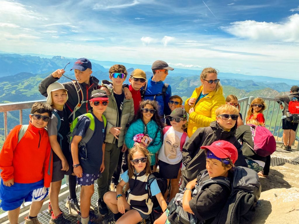 Group of campers in sunglasses posing at a mountain summit viewpoint above the valleys