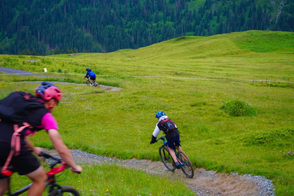 Two riders on a mountain bike trail winding across green alpine pastures