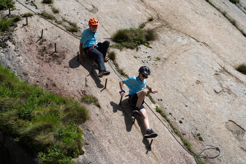 Two campers clipped in on a via ferrata rock slab with iron rungs