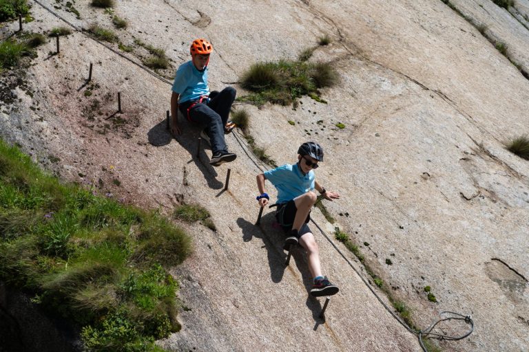 Two campers clipped in on a via ferrata rock slab with iron rungs