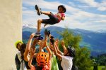 Campers in bike helmets tossing a friend into the air in celebration in the mountains