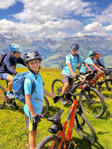Junge Camper mit ihren Mountainbikes auf einer Blumenwiese über dem Tal