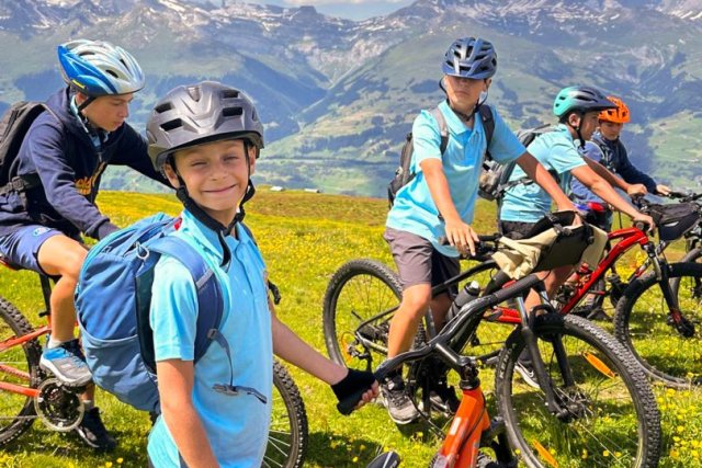 Junge Camper mit ihren Mountainbikes auf einer Blumenwiese über dem Tal