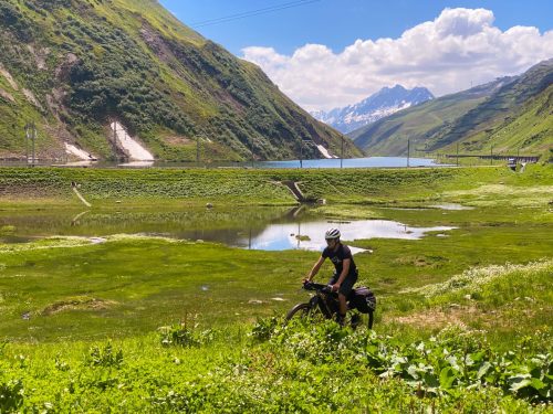 Bike Travel Camp rider passing an alpine lake on a mountain pass in Switzerland