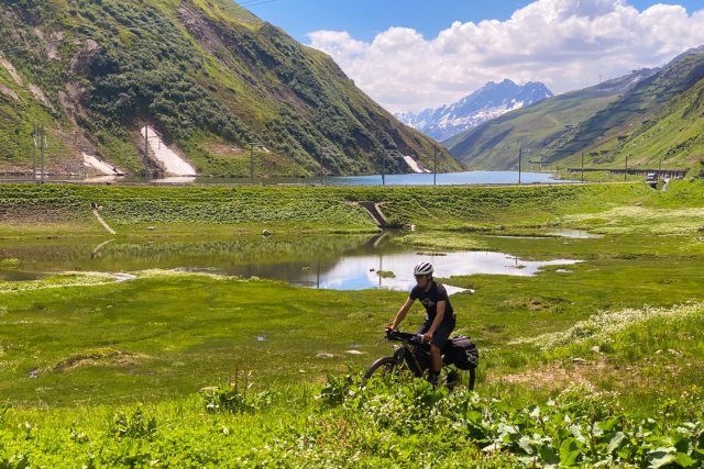 Bike Travel Camp rider passing an alpine lake on a mountain pass in Switzerland