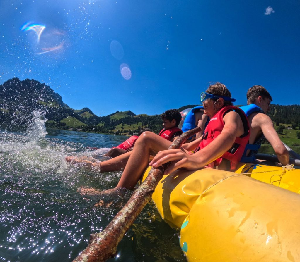 Children in life jackets splashing from a raft on an alpine lake at summer camp in Switzerland