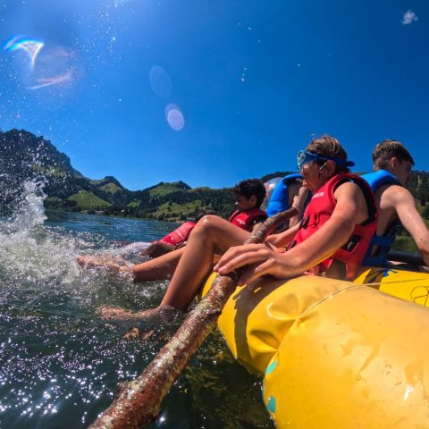 Children in life jackets splashing from a raft on an alpine lake at summer camp in Switzerland