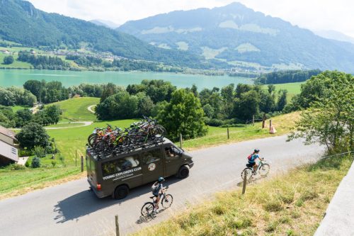 Van d'assistance Young Explorers Club chargé de vélos escortant de jeunes cyclistes au bord d'un lac