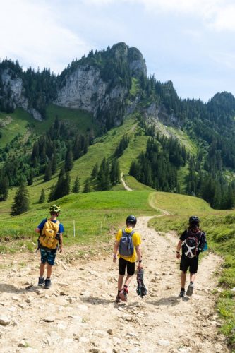 Three children hiking a mountain trail towards a rocky peak