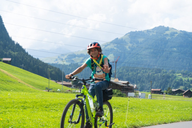 Young camper waving from her bike on a road through alpine meadows