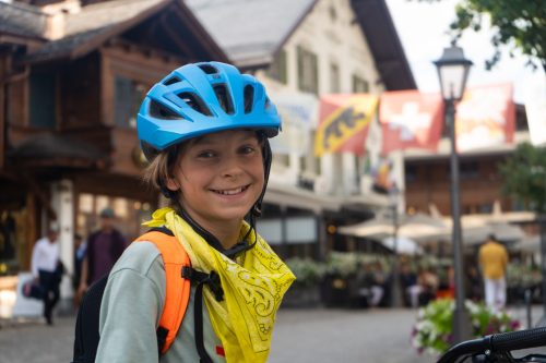 Smiling young cyclist in a blue helmet in the village of Gstaad
