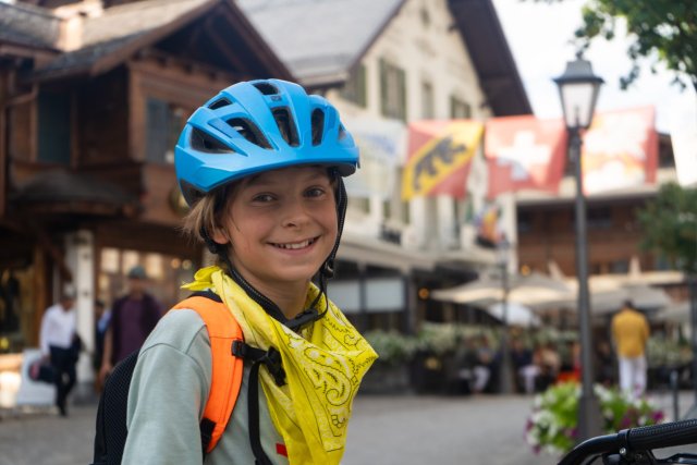 Smiling young cyclist in a blue helmet in the village of Gstaad