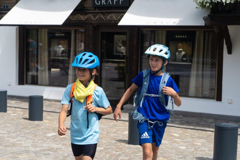 Deux jeunes cyclistes casqués marchant dans le centre du village de Gstaad