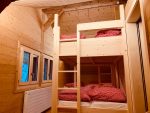 Lits superposés en bois aux duvets à carreaux rouges dans le dortoir du chalet des ados aux Diablerets