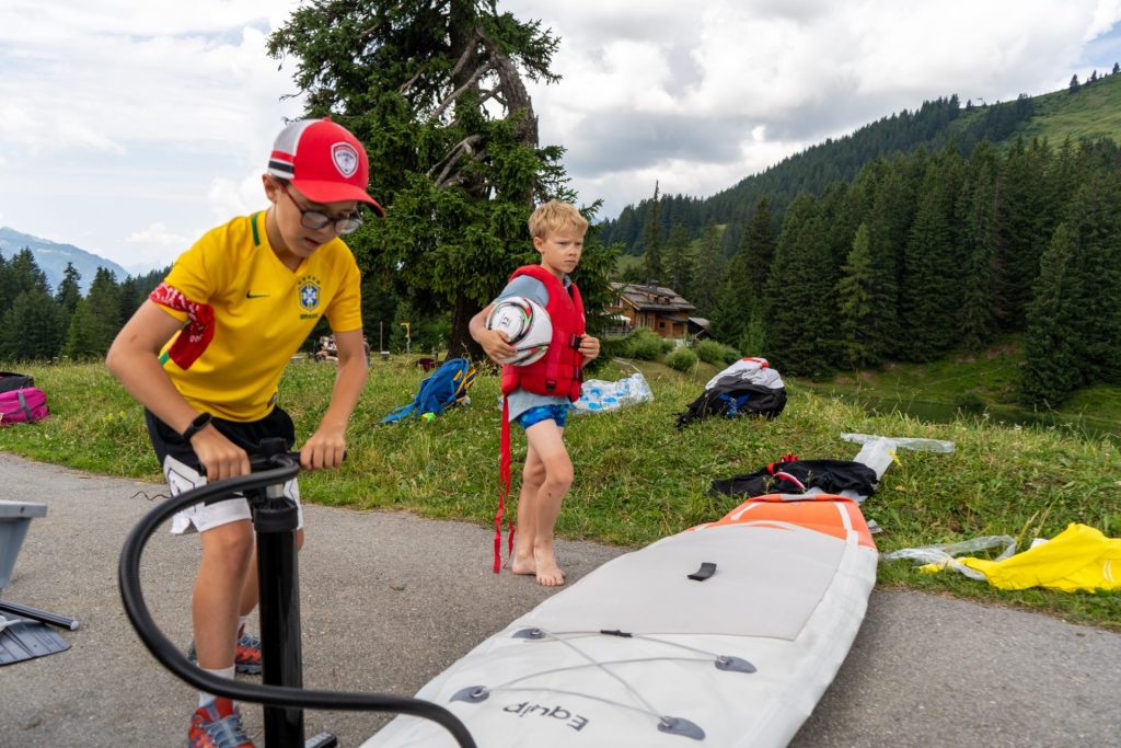 Campers pumping up a stand-up paddleboard beside the lake in the mountains
