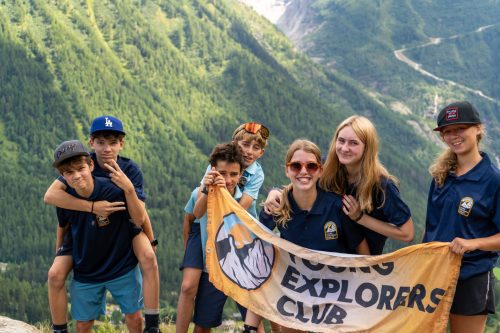 Teenagers holding a Young Explorers Club banner on a mountain pass during the Tour du Mont Blanc camp