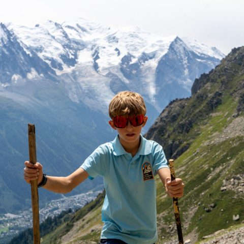 Young hiker with walking sticks in front of the snow-capped Mont Blanc massif