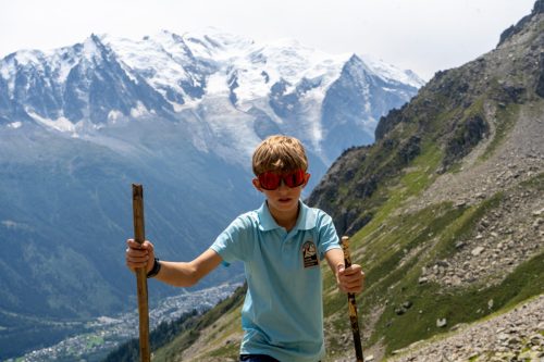 Young hiker with walking sticks in front of the snow-capped Mont Blanc massif
