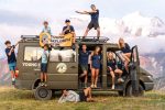 Teenagers posing on and around the Young Explorers Club van in the mountains during a travel camp