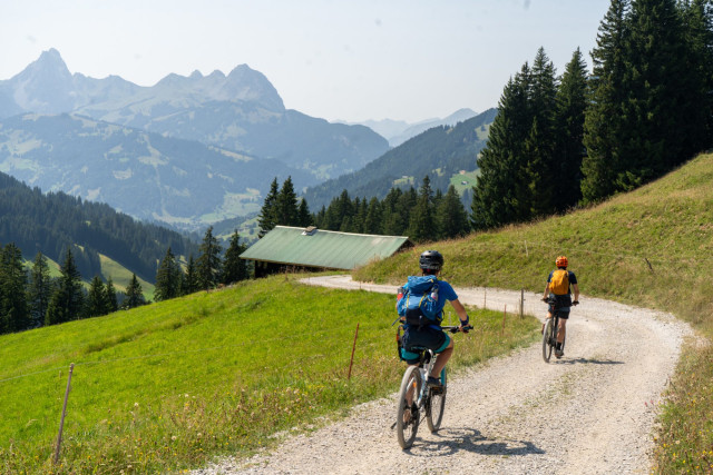 Two riders on a gravel track with the jagged Gastlosen peaks behind