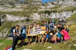 Grupo de adolescentes con mochilas de senderismo sosteniendo la pancarta del Young Explorers Club bajo acantilados calcáreos