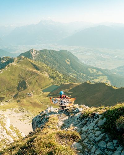 Hiker holding the Young Explorers Club banner on a ridge above the Rhône valley