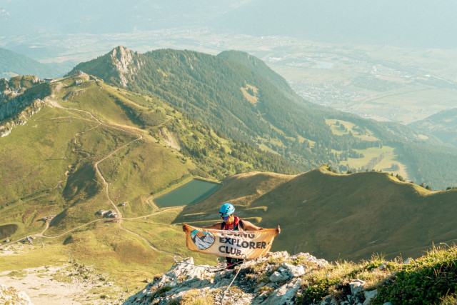 Hiker holding the Young Explorers Club banner on a ridge above the Rhône valley