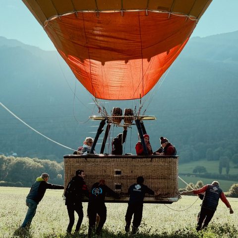 Campers and staff holding a hot air balloon basket before take-off in the Swiss Alps