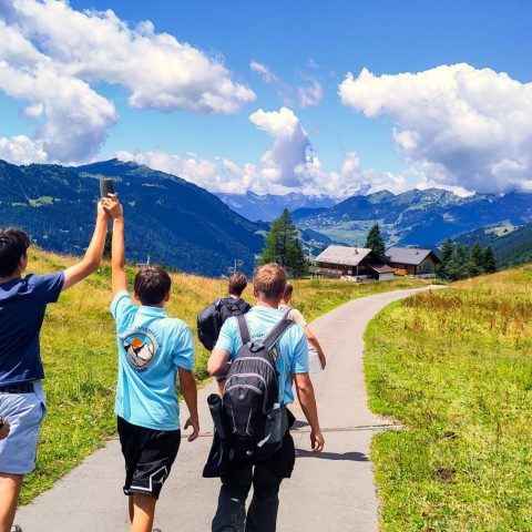 Group of teenagers in Young Explorers Club shirts hiking a path through an alpine valley
