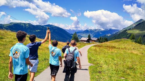 Group of teenagers in Young Explorers Club shirts hiking a path through an alpine valley