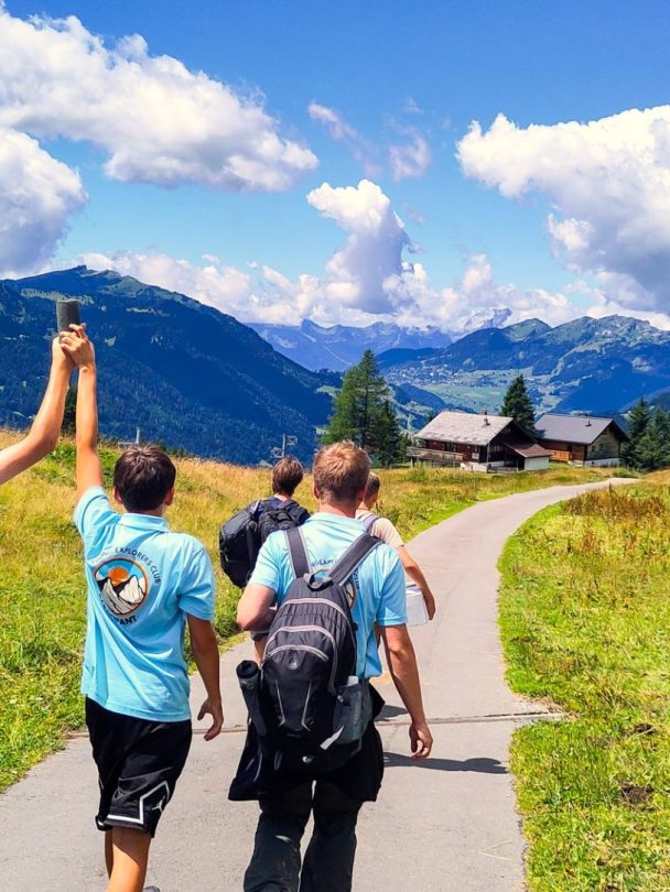 Group of teenagers in Young Explorers Club shirts hiking a path through an alpine valley