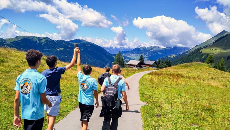 Group of teenagers in Young Explorers Club shirts hiking a path through an alpine valley
