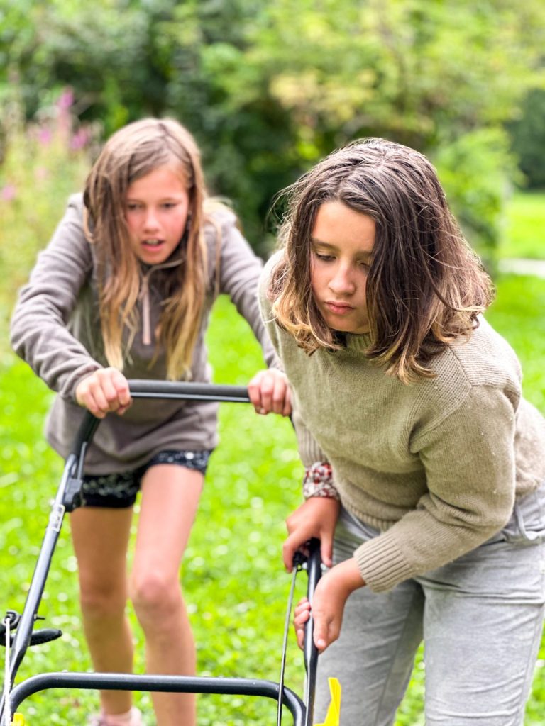 Two girls pushing a mower together in the chalet garden