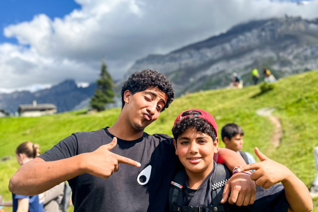 Two teenage campers posing on a mountain trail with the Alps behind them