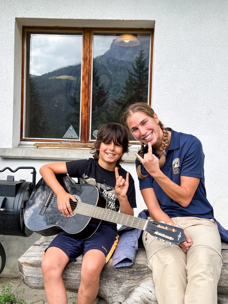 Campeur jouant de la guitare à côté d'une monitrice devant le chalet
