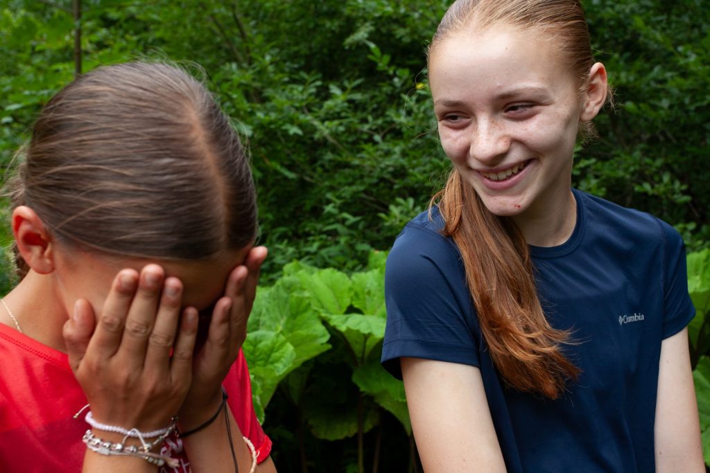 Zwei Mädchen lachen bei einem Spiel im Wald im Sommercamp
