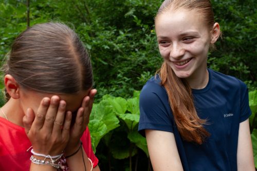 Zwei Mädchen lachen bei einem Spiel im Wald im Sommercamp