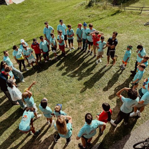 Campers standing in a circle on the grass for a group game at summer camp in Switzerland
