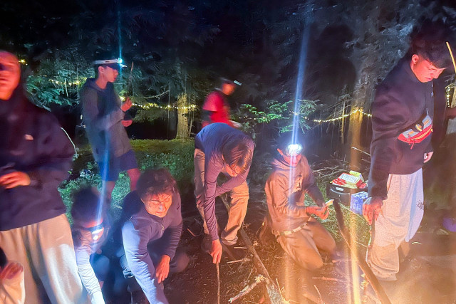 Campers with headlamps gathered around a campfire at night at the Survival Academy camp